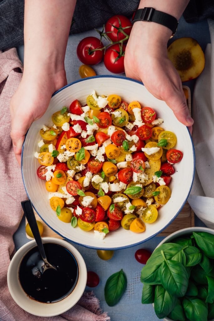 person holding plate of sliced tomato and green vegetable salad